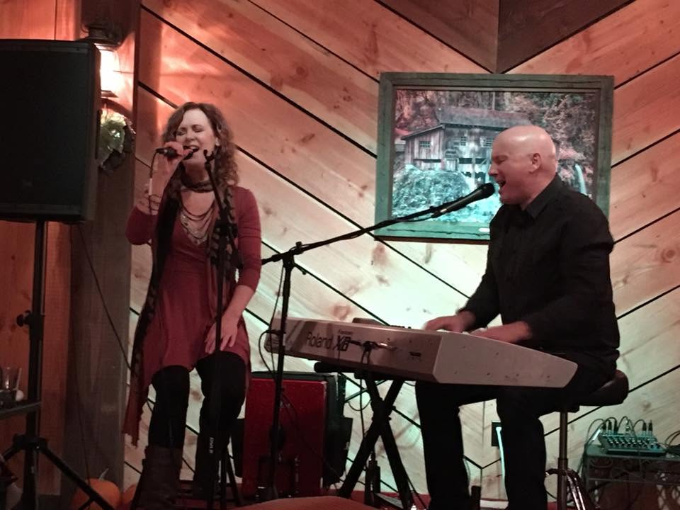Eric and Lauri performing together at a cabin-style venue, Eric on keyboard and Lauri singing